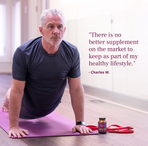 Older man with grey hair wearing a dark athletic shirt performing an upward-facing yoga pose on a purple mat in a bright indoor space.